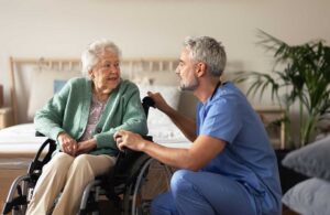 Older resident choosing clothing with a caregiver in a bright, private assisted living room.